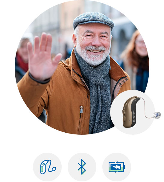 Kobieta z siwymi włosami spoglądająca w lustro, obok aparat słuchowy z funkcją Bluetooth.