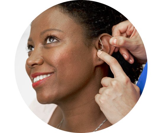 Een audioloog plaatst een onzichtbare gehoorapparaat achter het oor van een patiënt, te herkennen aan een professionele klinieksetting. Mogelijk afkomstig van Audika, gespecialiseerd in gehoorzorg.