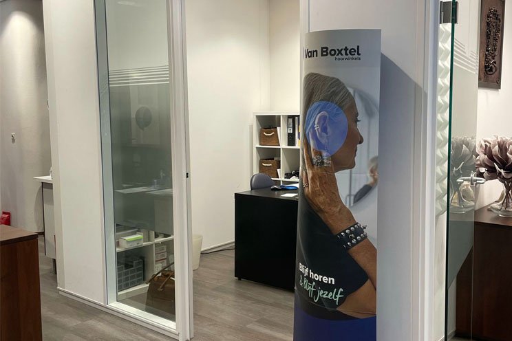 Audika in Hoorn met poster van persoon die een hoortoestel aanpast.