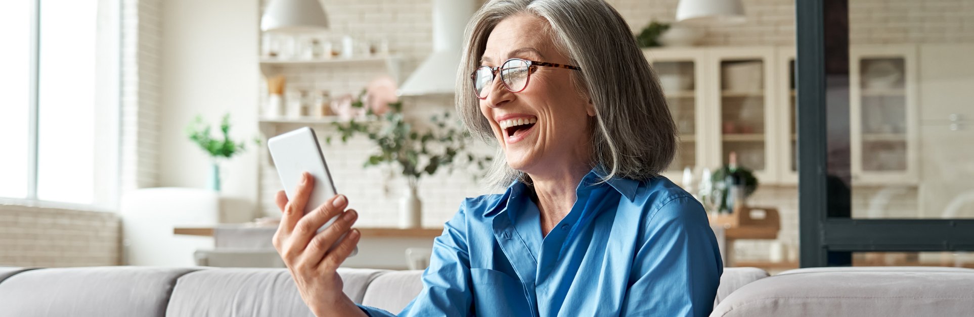 Lachende Frau mit blauer Bluse und Smartphone KIND AUDIKA