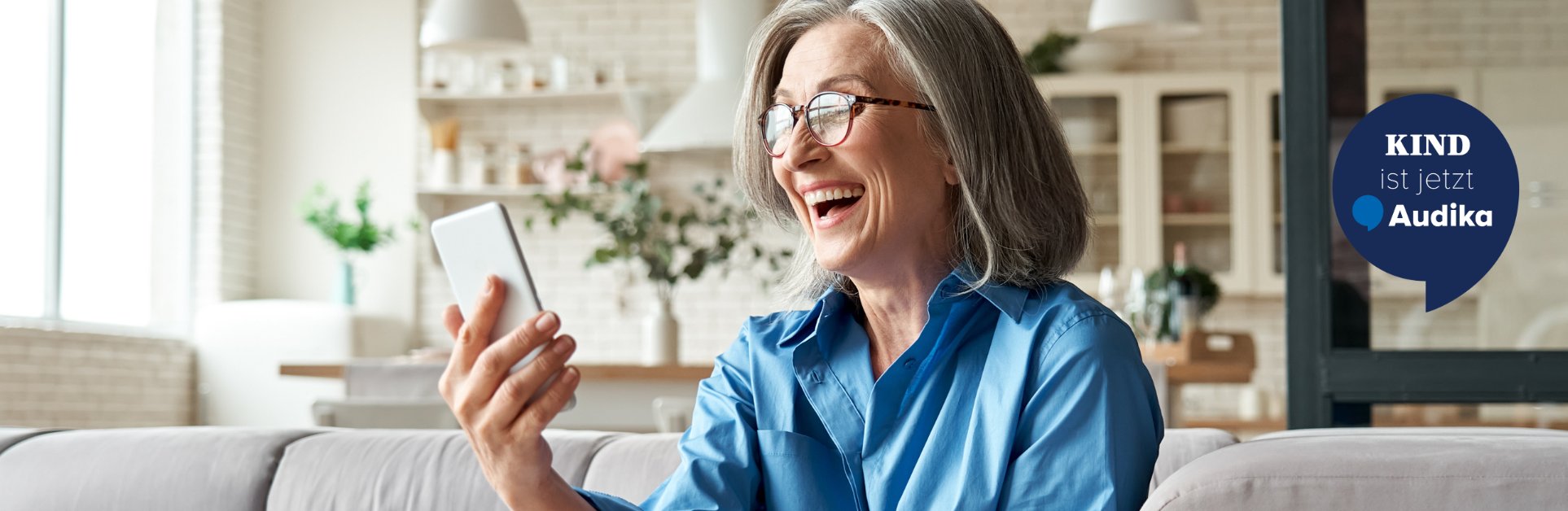 KIND ist jetzt Audika. Frau Lachen mit Smartphone in der Hand. 