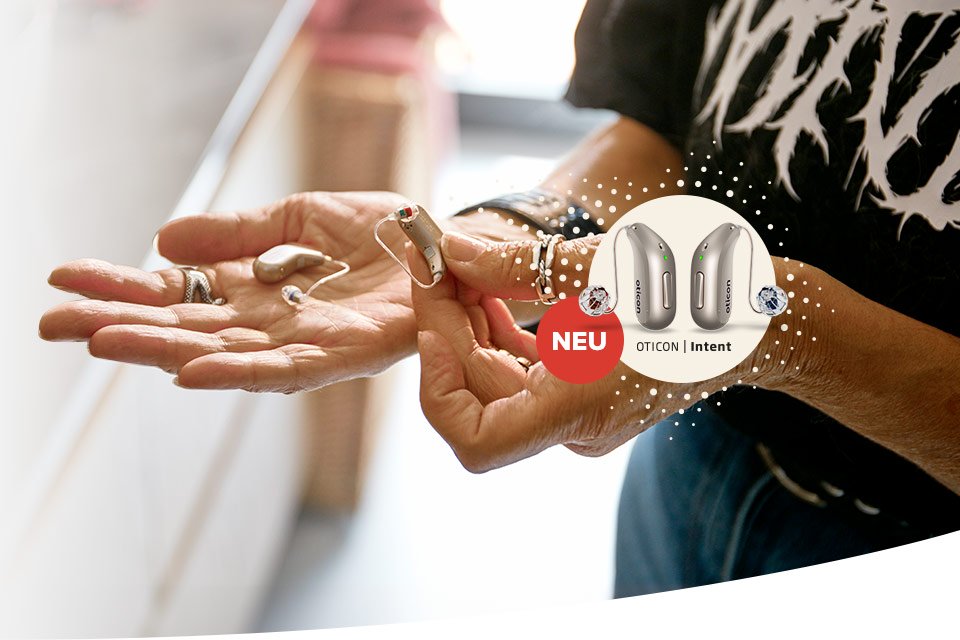 Hände halten moderne Hörgeräte von Oticon, umgeben von einem stilvollen, hell beleuchteten Raum. Text: ’NEU OTICON | Intent’, begleitet von Produktabbildungen der Hörgeräte und einem roten Hinweis.