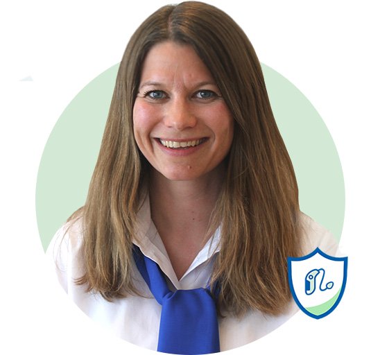 Eine Person mit braunen, schulterlangen Haaren trägt eine weisse Bluse und eine blaue Krawatte. Im Vordergrund rechts unten erscheint ein blau-weisses Wappensymbol mit einem stilisierten Ohr. Der grüne Kreis im Hintergrund verleiht dem Bild einen professionellen, neutralen Kontext.