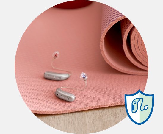 Zwei moderne Hörgeräte auf einer rosa Yogamatte mit gerollter Kante.