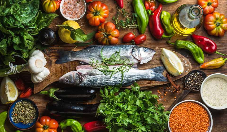 Poissons frais sur une planche entourés d'ingrédients colorés comme légumes, herbes, lentilles et épices.