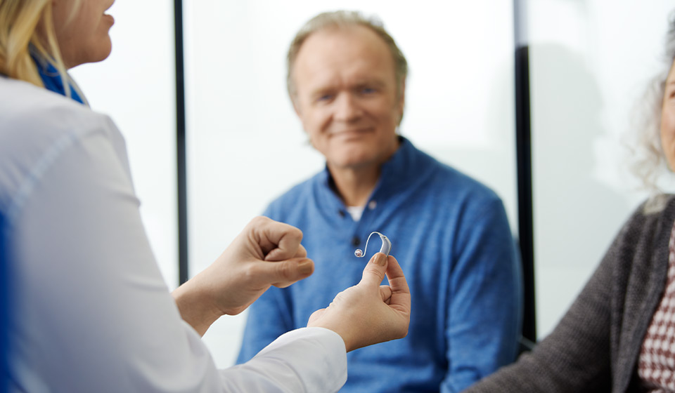 Une audioprothésiste présentant un appareil auditif à des patients lors d’une consultation.