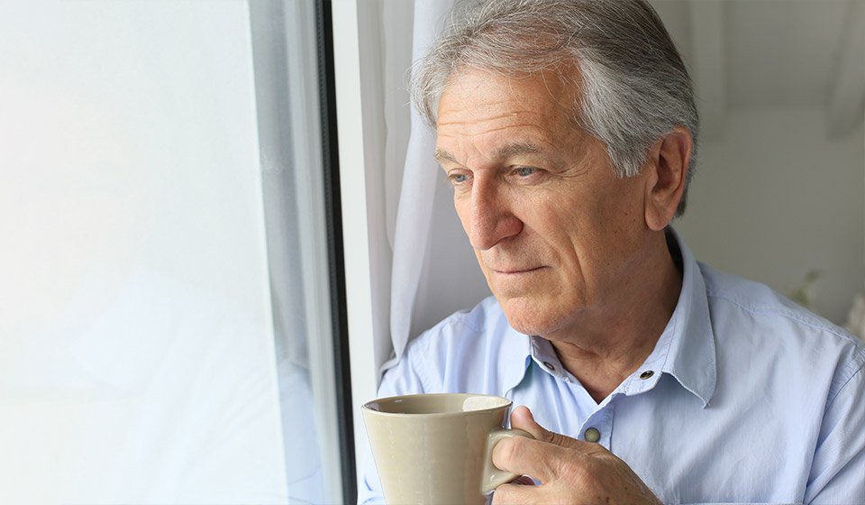 Homme senior tenant une tasse de café tout en regardant par la fenêtre.