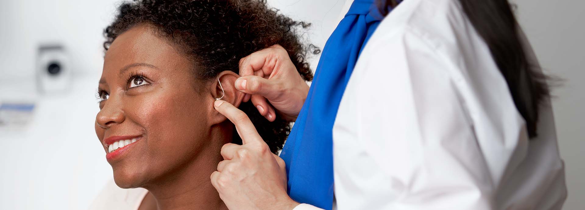 L’image montre une femme à qui l’on place un appareil auditif derrière l’oreille