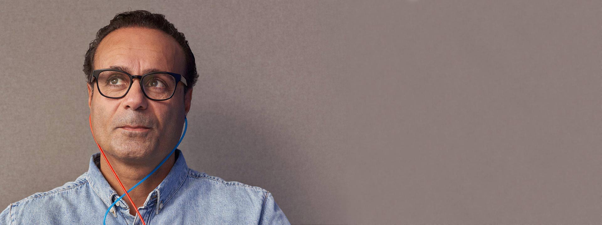 Un homme portant un casque audio bleu avec un cordon rouge et bleu, habillé d’une chemise en denim.