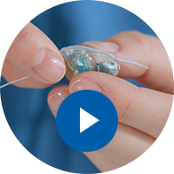 L’image montre des mains qui changent la pile d’un appareil auditif