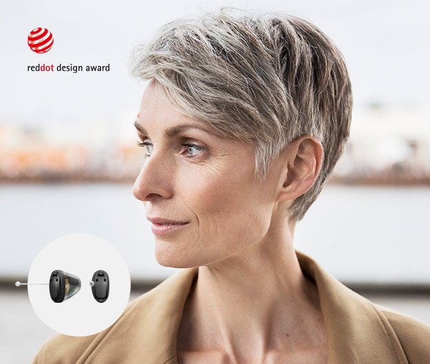 Des appareils auditifs modernes avec design primé portés par une femme aux cheveux gris dans un environnement urbain flou.