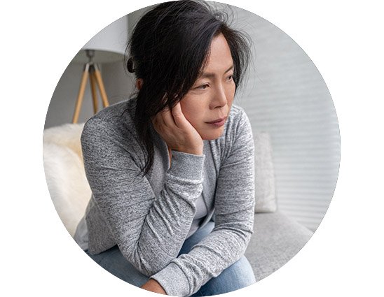 Femme pensive assise sur un canapé dans un intérieur lumineux.