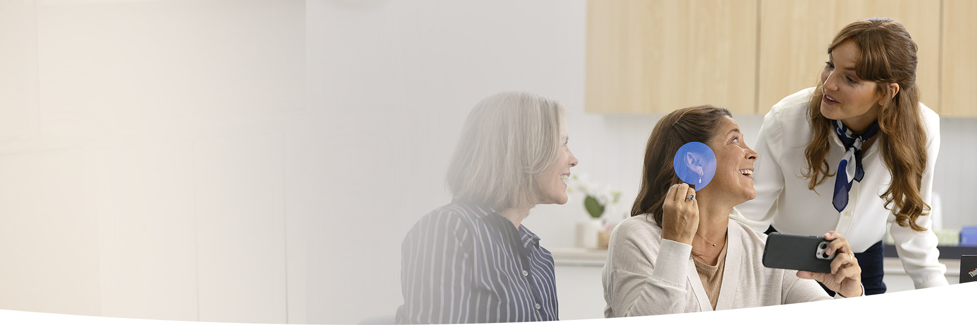 Deux audioprothésistes discutent avec une patiente qui tient un appareil auditif.