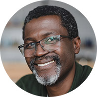 Un homme souriant, portant des lunettes, en arrière-plan flou.