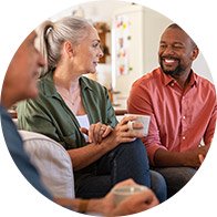 Des personnes discutent dans un salon lumineux, assises sur des canapés, avec des tasses de café en main. Une ambiance conviviale et chaleureuse se dégage. Aucun texte visible.