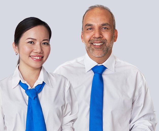 Deux personnes vêtues de chemises blanches avec des cravates bleues sur un fond uni. Leurs visages sont floutés, sans indication explicite de marque ou de texte dans l’image.