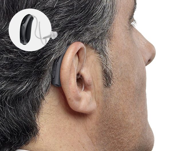 Un contour d’oreille auditif noir est installé derrière l’oreille d’un homme aux cheveux gris, avec un embout translucide dans le conduit auditif. Un médaillon montre le même appareil.