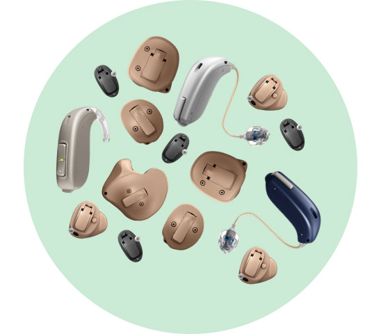 Des appareils auditifs de diverses formes et couleurs (beige, noir, argenté, bleu), comprenant des modèles intra-auriculaires et contour d’oreille, sont disposés sur un fond vert clair uniforme.