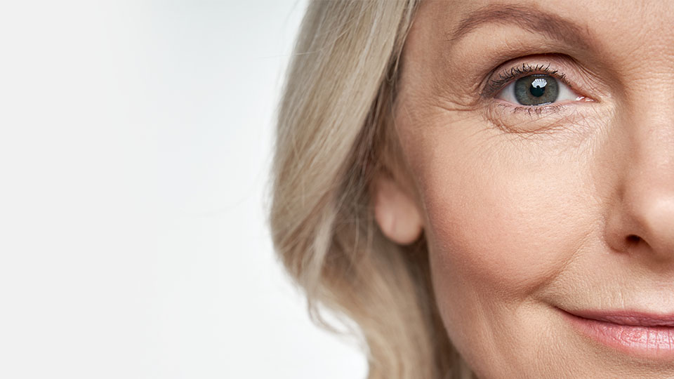 Un orecchio femminile evidenziato con capelli biondi che cadono morbidamente intorno, su sfondo bianco sfocato. Nessun apparecchio acustico o testo visibile nell’immagine.