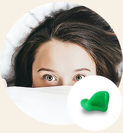 Un dispositivo acustico verde brillante è posizionato su uno sfondo beige circolare. Accanto, capelli castani sciolti suggeriscono la presenza di una persona parzialmente visibile. Nessun testo individuabile.