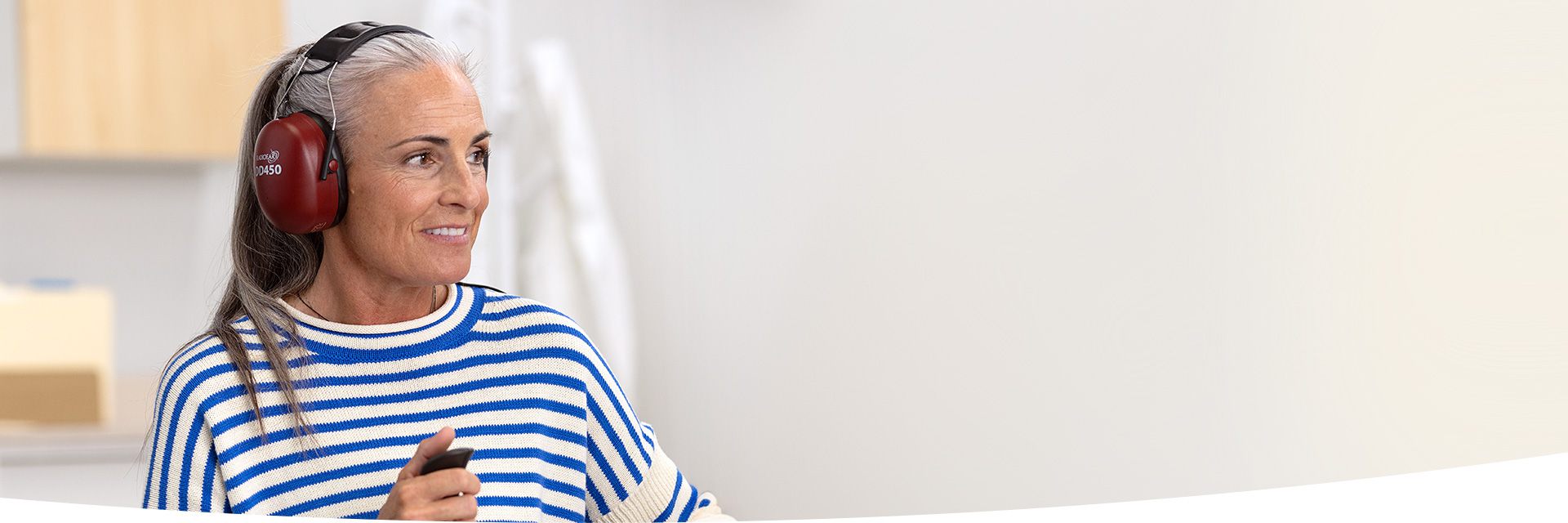 Donna con capelli grigi indossa protezioni auricolari rosse in un ambiente interno.