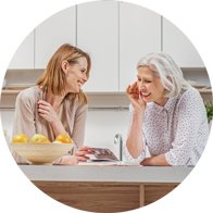 Due donne, una giovane e una anziana, conversano in cucina. La donna anziana, con capelli bianchi, sembra indossare un apparecchio acustico. Sul tavolo ci sono limoni in una ciotola.