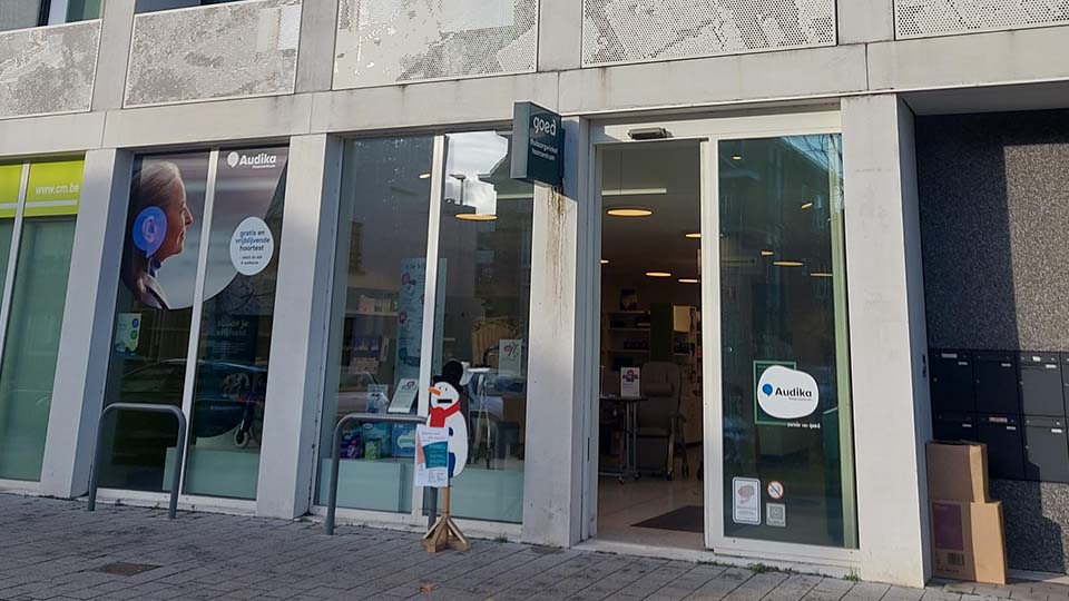 De gevel van een Audika gehoorcentrum met glazen deuren en ramen; binnenin zijn stoelen en audiologische apparatuur zichtbaar. Op het raam staat 'Audika, geef je gehoor de zorg.'