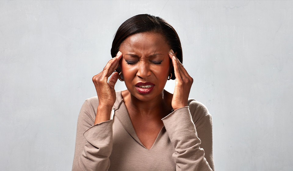 Vrouw houdt haar beide handen tegen haar hoofd, mogelijk last van oorsuizen of gehoorproblemen.