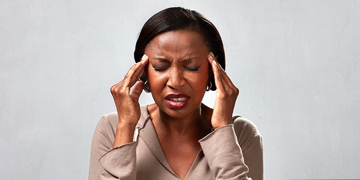 Vrouw met twee handen tegen haar slapen, mogelijk last van hoofdpijn of spanning.