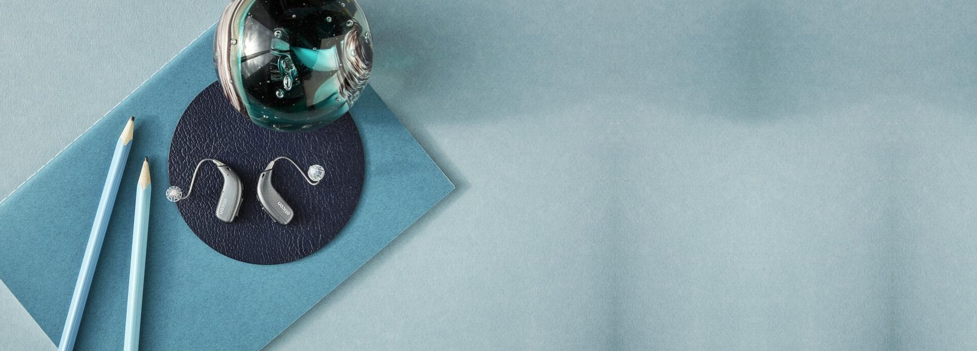 Twee moderne hoortoestellen met accessoires op een blauwe achtergrond