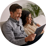 Man en vrouw die samen op een bank zitten en een tablet bekijken, met een plant op de achtergrond.