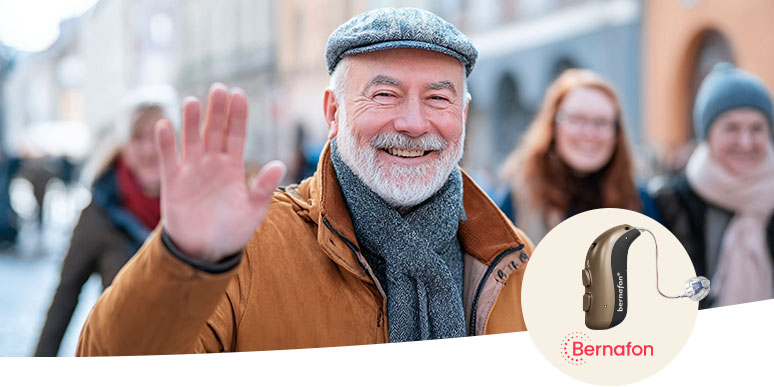 Een persoon met grijs haar kijkt in een spiegel, omringd door een neutrale achtergrond. Rechtsonder staat een Bernafon-hoortoestel afgebeeld met het Bernafon-logo, gericht op hoorzorg.