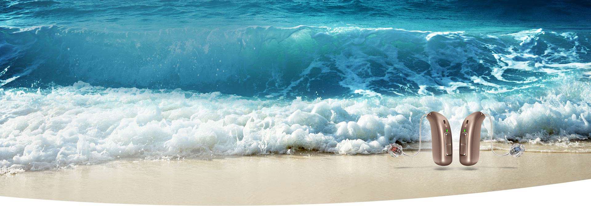 Twee huidkleurige hoortoestellen staan op een strand, met krachtige blauwe golven op de achtergrond. De scène benadrukt helder gehoor in een natuurlijke, dynamische omgeving; merknaam niet zichtbaar.