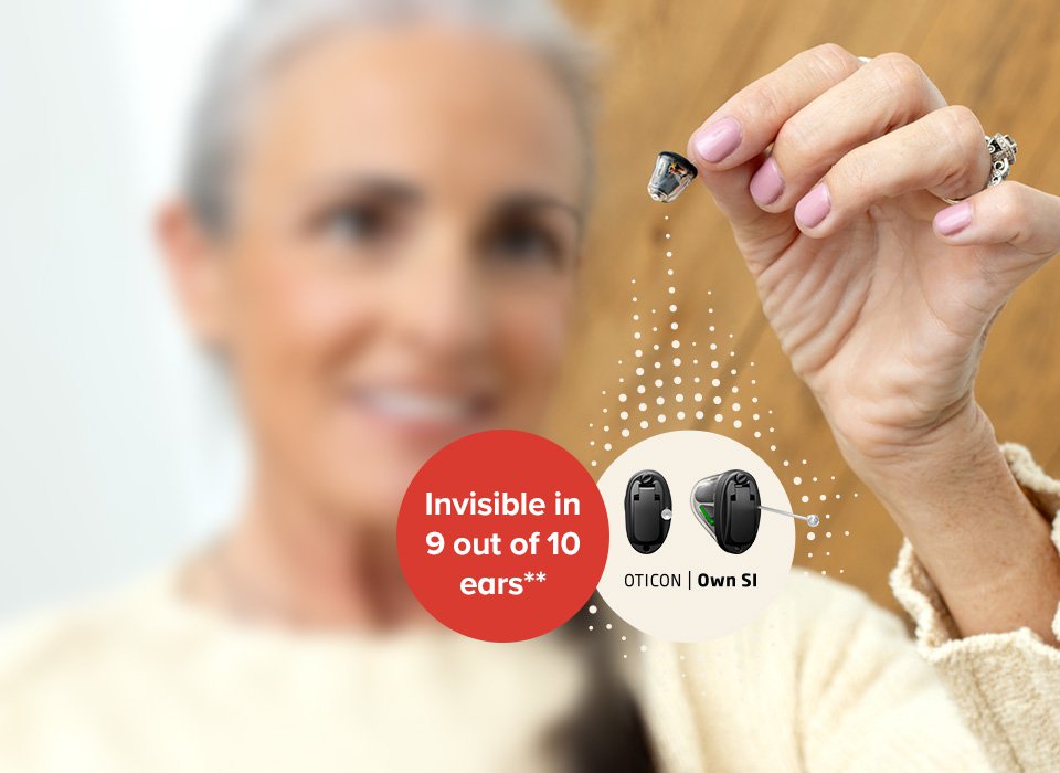 Een hand houdt een klein Oticon Own SI hoorapparaat vast. Tekst in beeld: ’9 out of 10 ears’’. Context: houten achtergrond, promotie van Audika hooroplossingen.